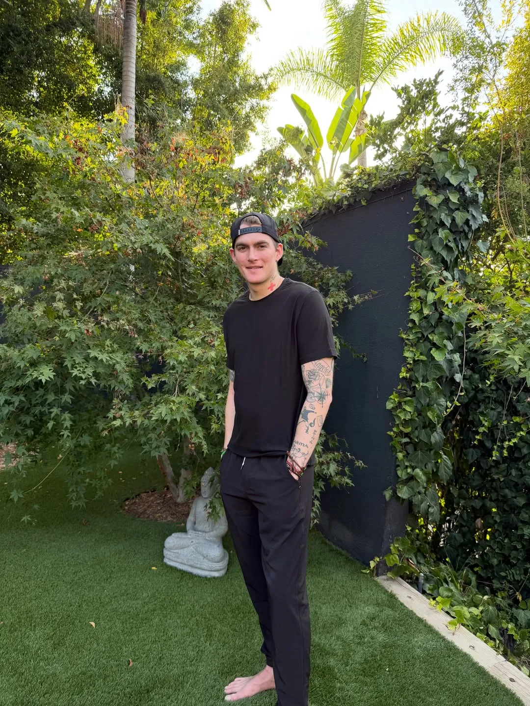 Presley Gerber standing barefoot in a garden with a Buddha statue in the background.
