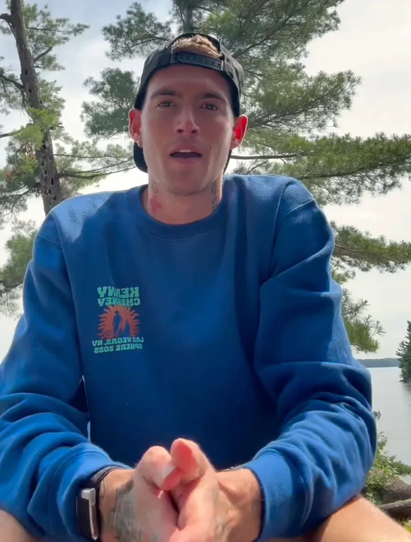 Presley Gerber wearing a blue sweatshirt and a backwards black cap, with trees and water in the background.