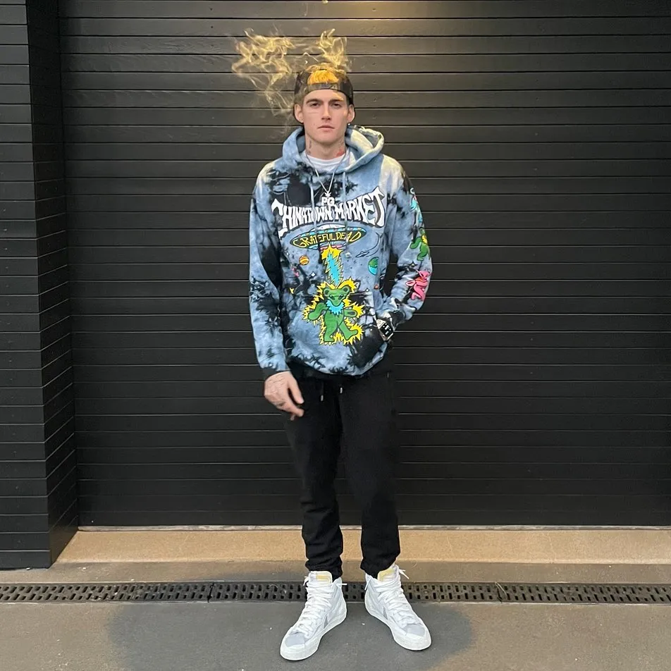 Presley Gerber wearing a tie-dye hoodie with a Grateful Dead graphic, black pants, and white sneakers.