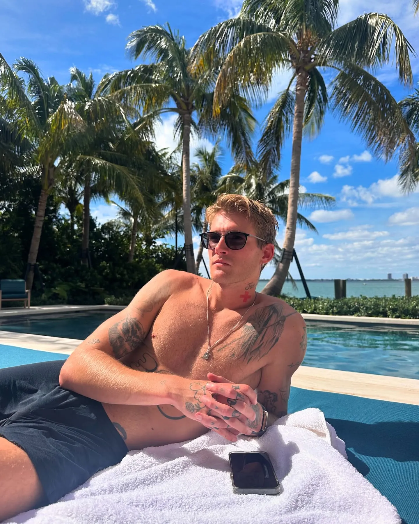 Presley Gerber lounging by a pool with palm trees in the background.