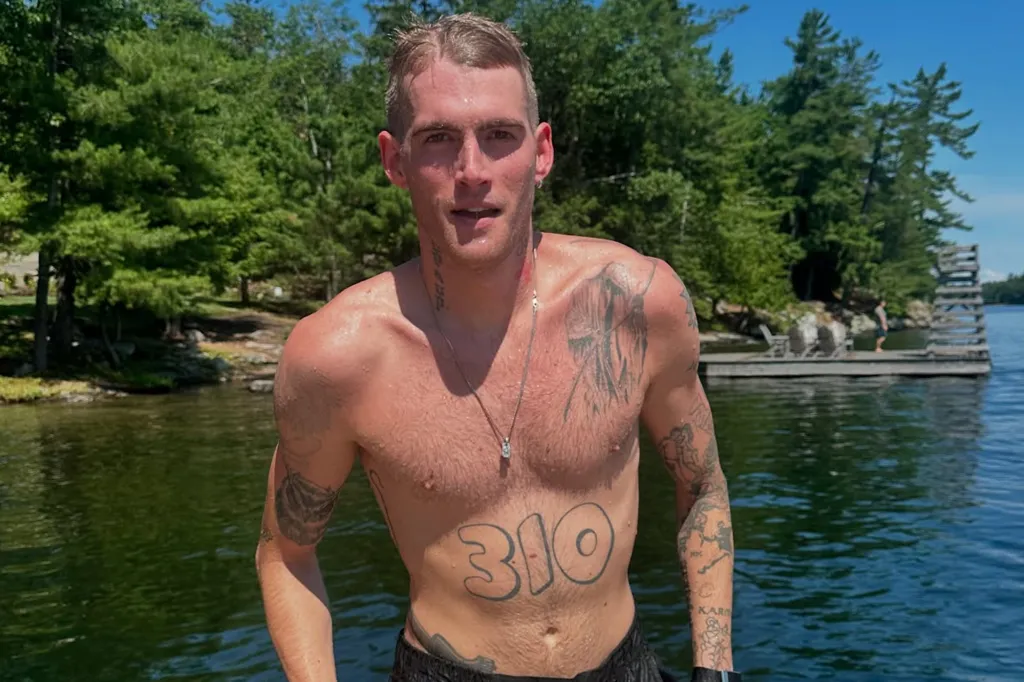 Presley Gerber, shirtless and wet, standing in a lake with trees and a dock in the background.