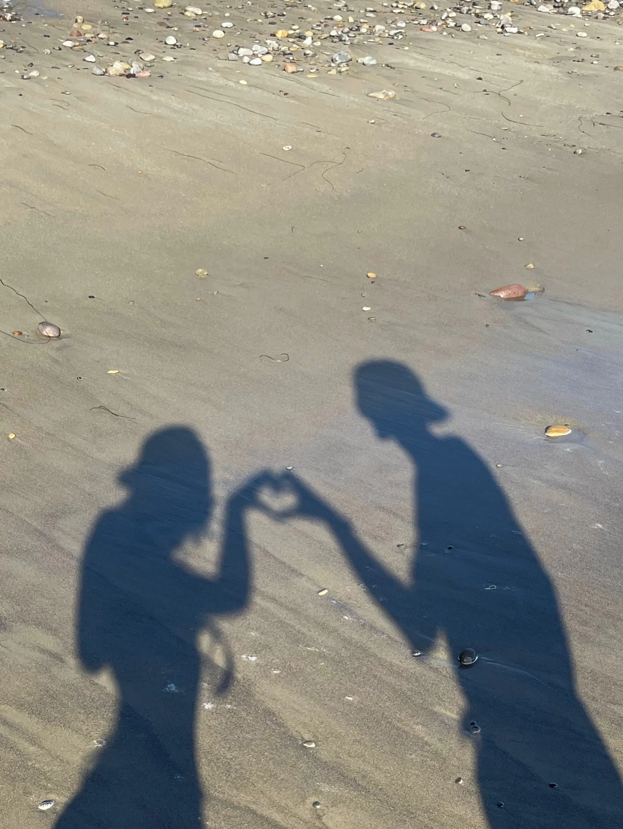 Shadows of two people on a sandy beach forming a heart with their hands.