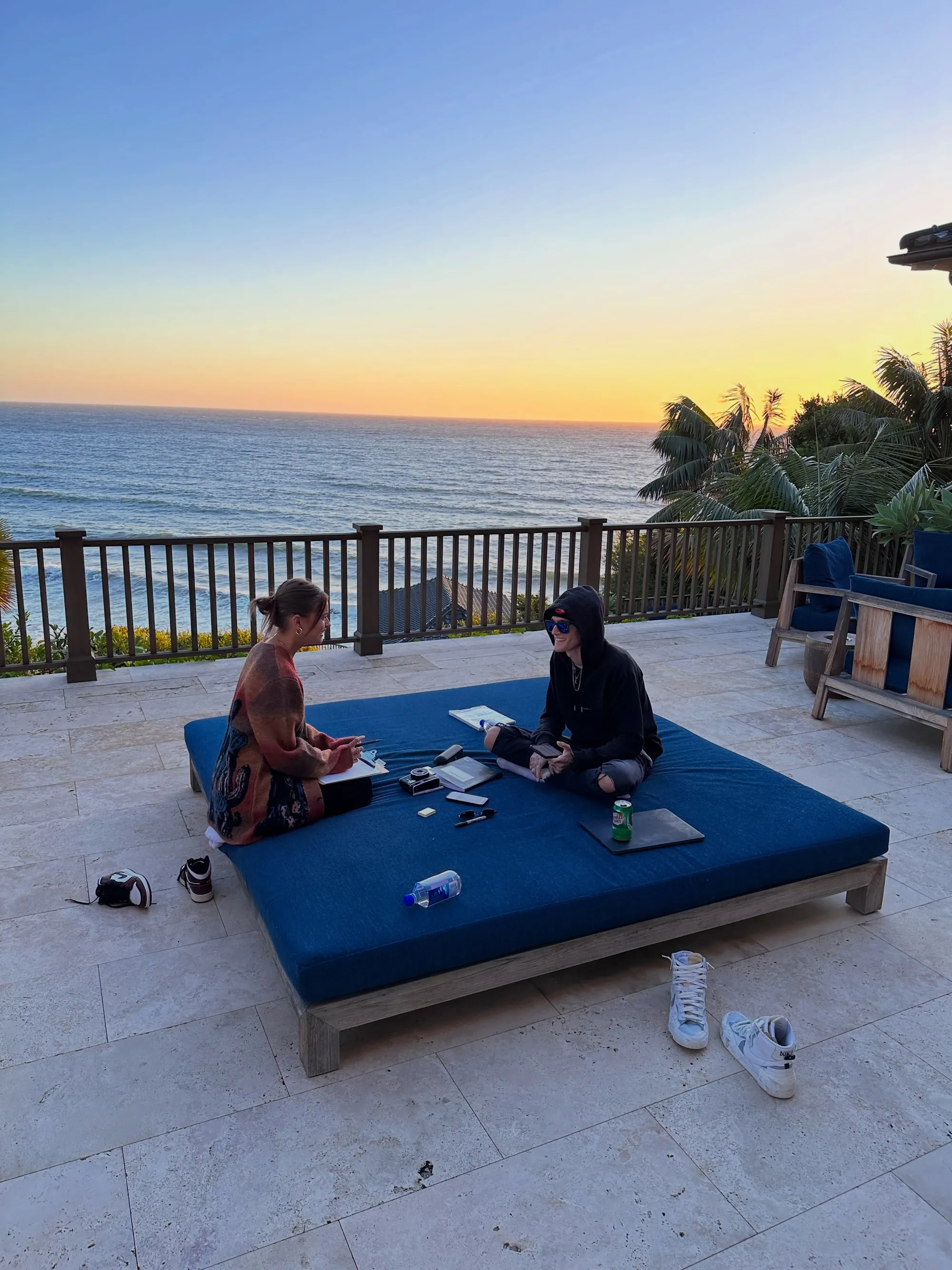 Lexi Wood and Presley Gerber sitting on an outdoor daybed at sunset overlooking the ocean.