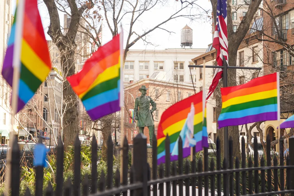 Pride flags fly in front of the American Flag near a statue at the Stonewall National Monument.