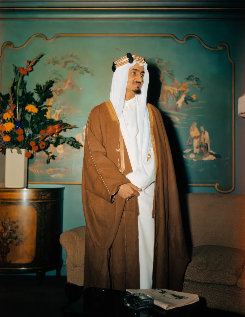 Prince Emir Faisal, second son of King Ibn Saud of Saudi Arabia, stands in front of a painting.