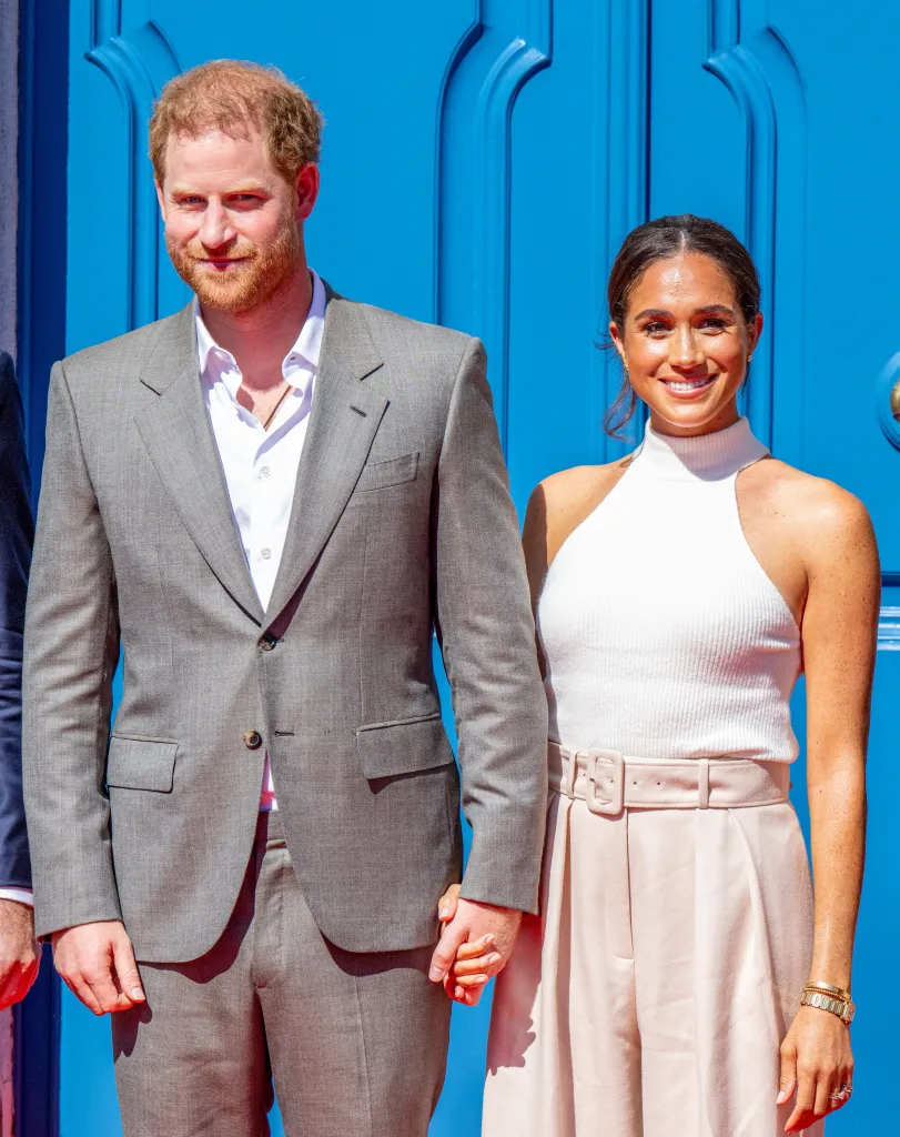 Prince Harry and Meghan Markle holding hands, standing in front of a blue door.