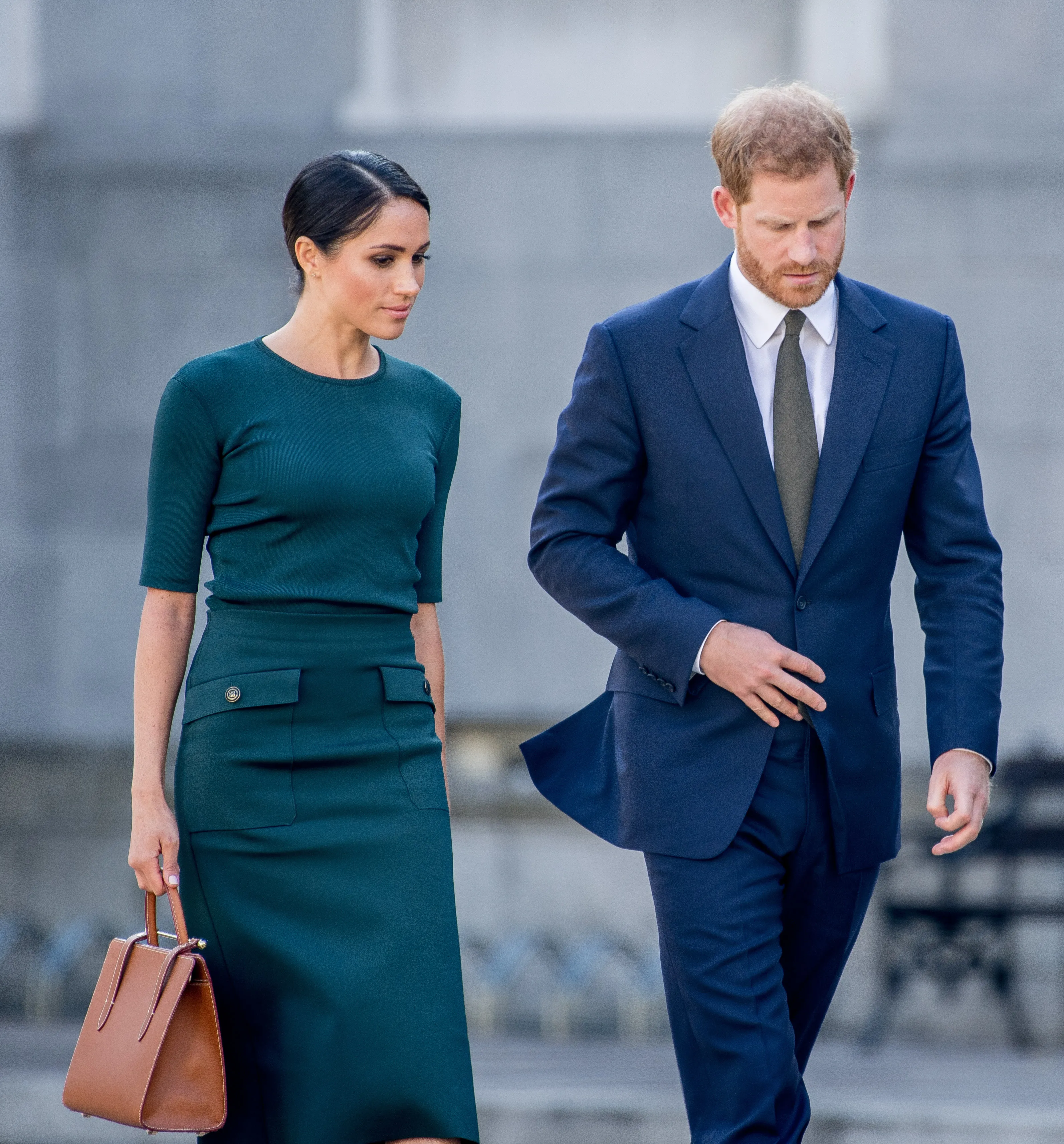 Meghan Markle and Prince Harry walking side-by-side, Meghan in a green dress and Prince Harry in a blue suit.