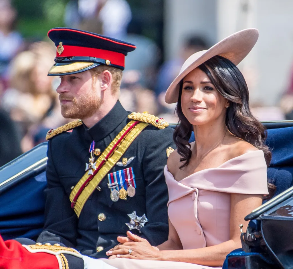 Prince Harry in military uniform and Meghan Markle in a pink dress and hat, sitting in a carriage.