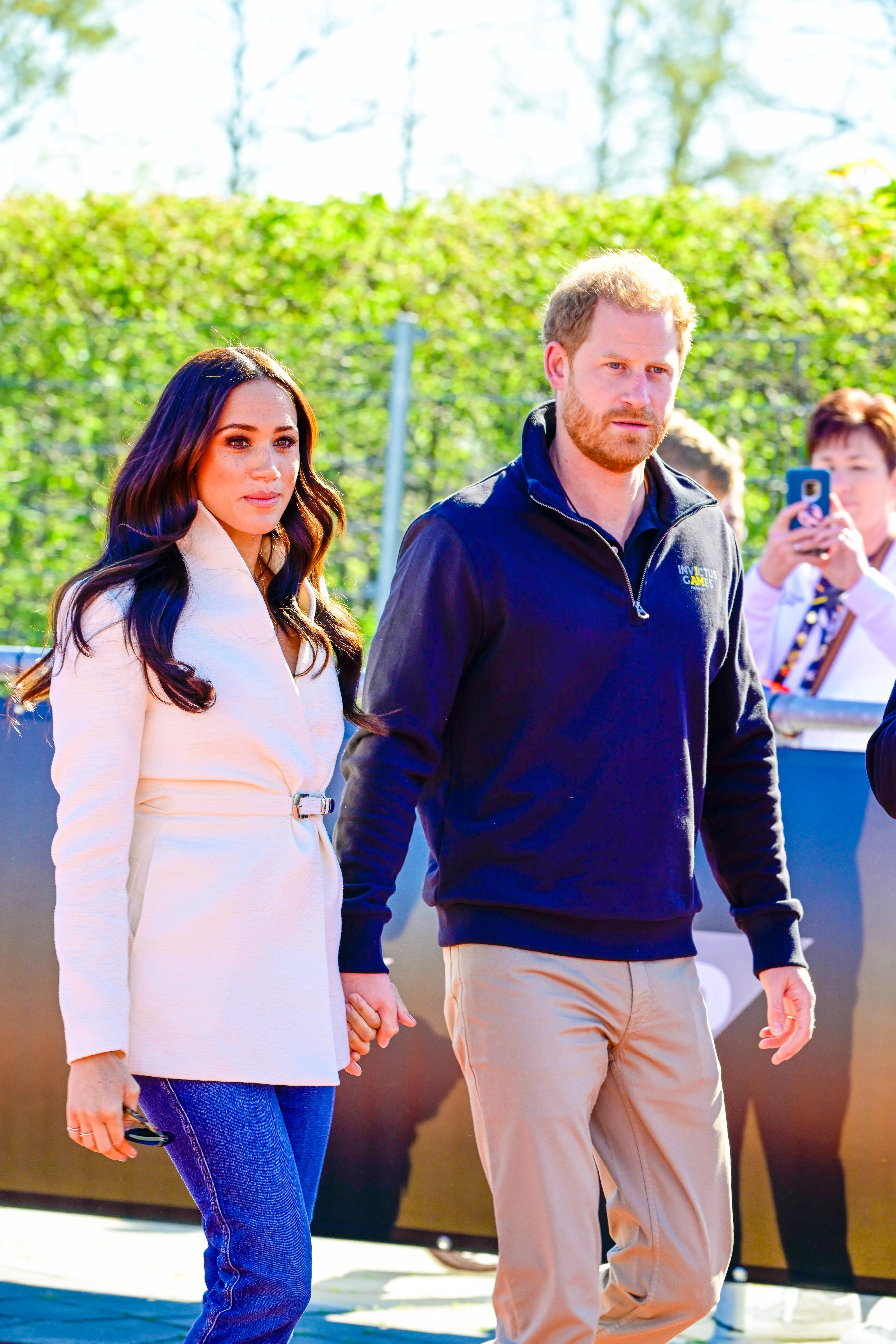 Prince Harry and Meghan Markle holding hands as they walk outdoors.