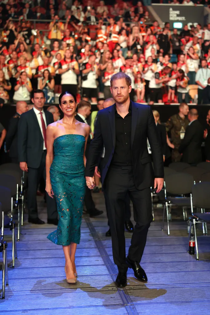 Prince Harry and Meghan Markle holding hands while walking through an arena.