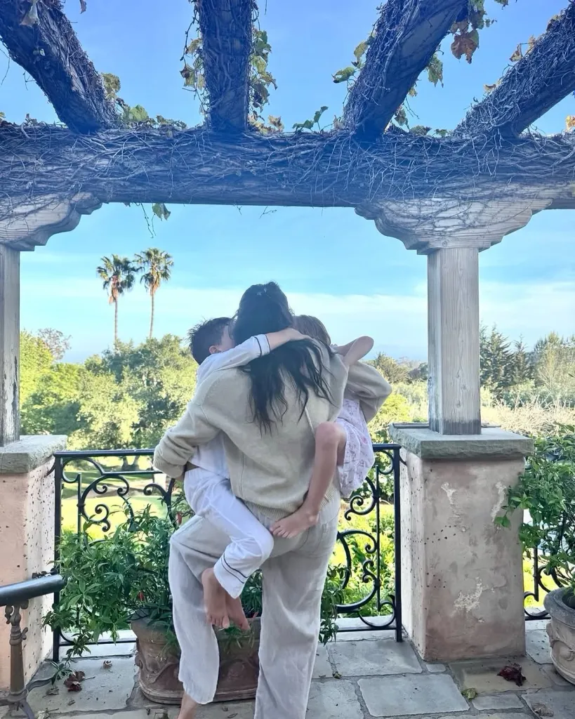 Meghan Markle hugging her children, Prince Archie and Princess Lilibet, on a balcony.