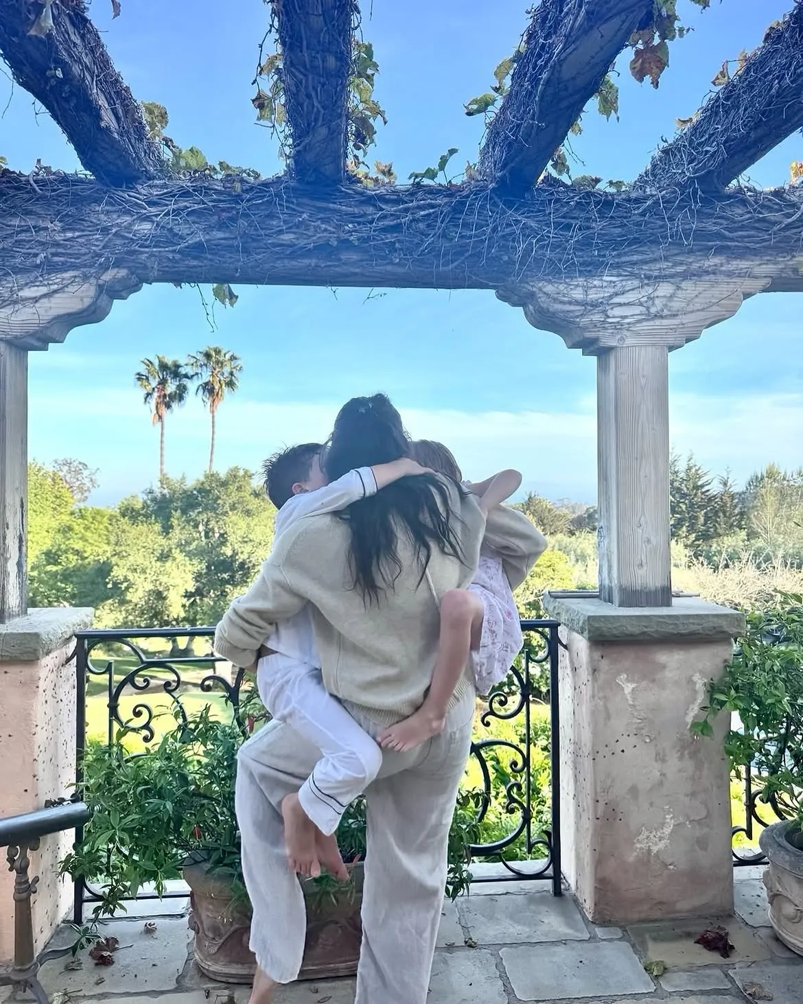 Meghan Markle hugging Prince Archie and Princess Lilibet on a balcony.