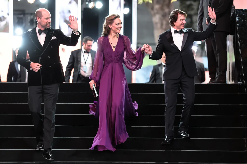 Prince William, in a black tuxedo, Catherine, Princess of Wales, in a purple gown, and Tom Cruise , in a black tuxedo, walking down stairs and waving to the public.