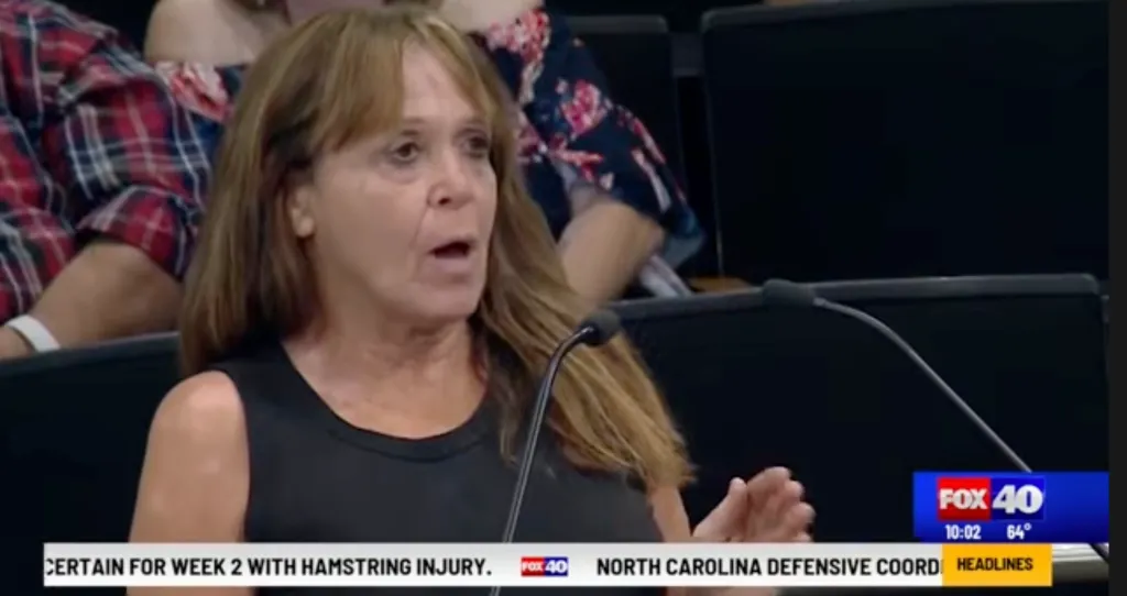 A woman speaking at a microphone during a public meeting, likely about the proposed slaughter facility.