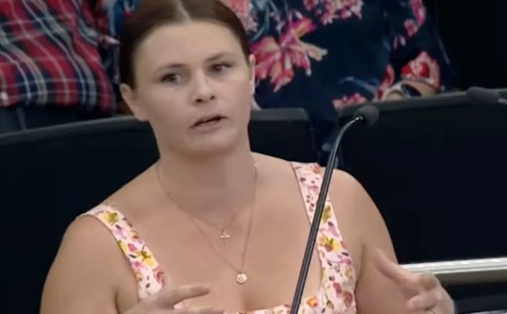 A woman in a floral top speaks at a microphone.