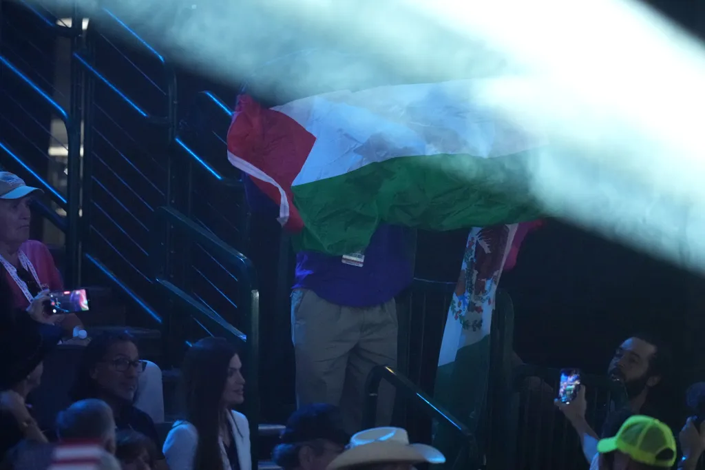 Protester holding a Palestinian flag at the Republican convention, with a Mexican flag hanging from the railing below.