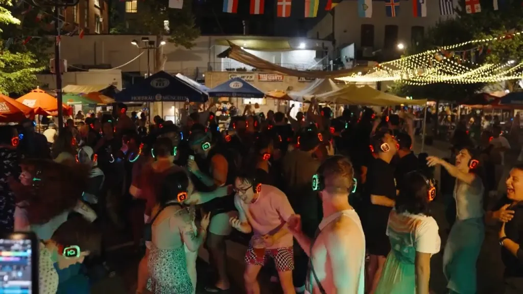 A crowd of people wearing glowing headphones dances at a Silent Disco event at Bohemian Beer Garden.