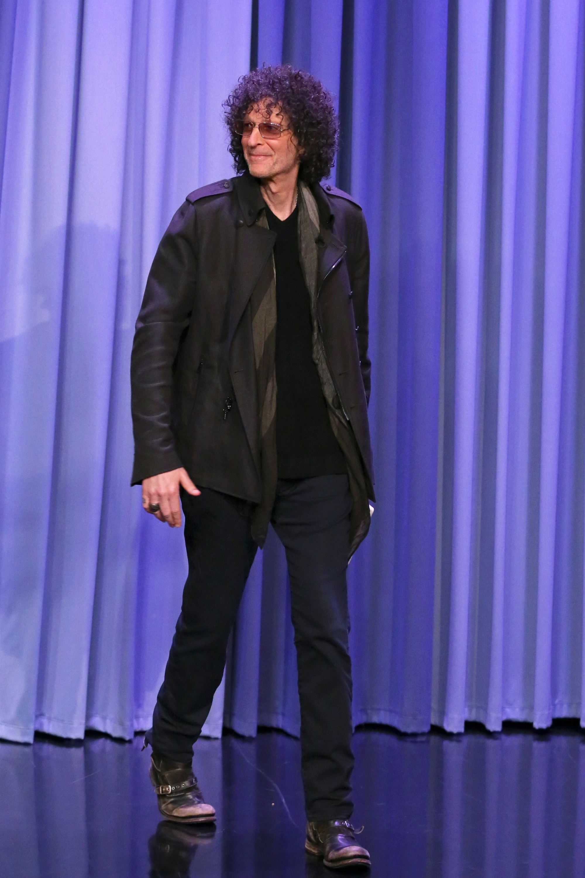 Howard Stern walking in sunglasses, a dark coat, and black pants.