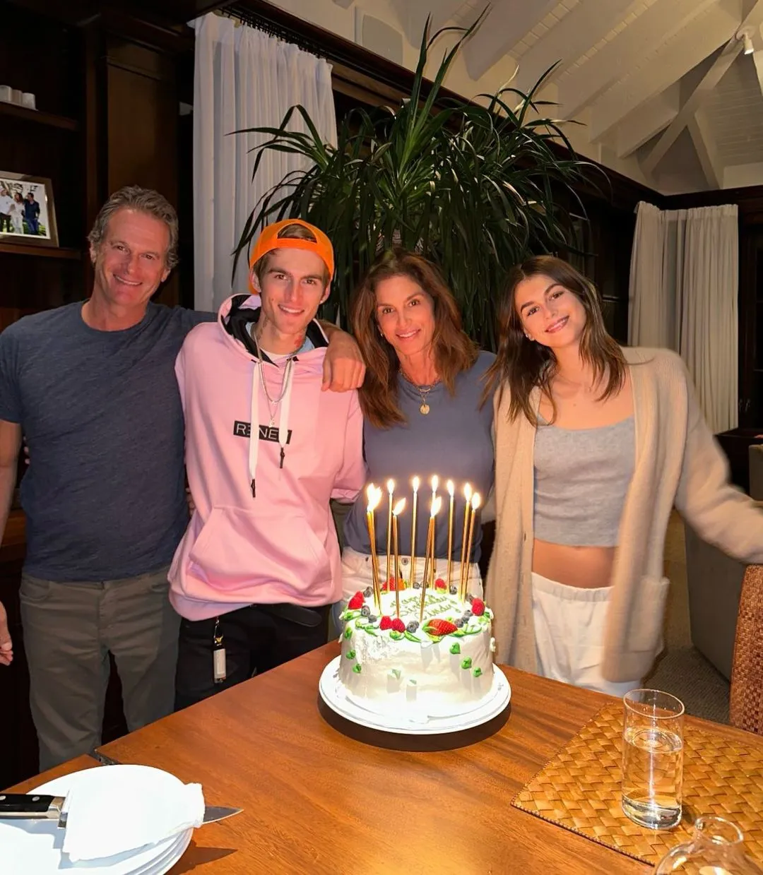 Rande Gerber, Presley Gerber, Cindy Crawford, and Kaia Gerber standing together behind a birthday cake with lit candles.