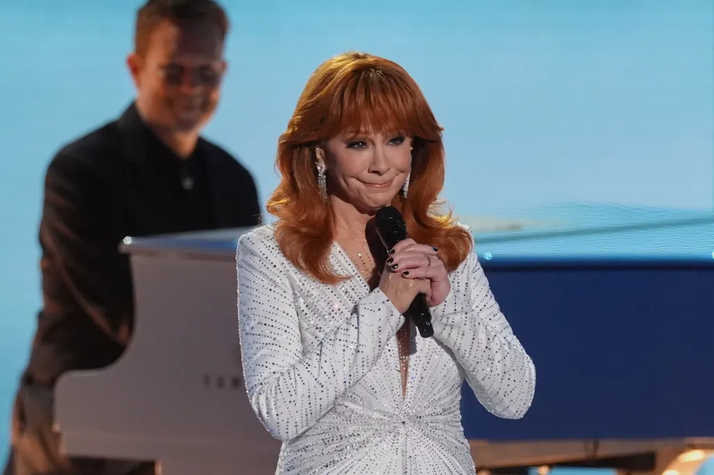 Reba McEntire in a white sequined dress holds a microphone while performing
