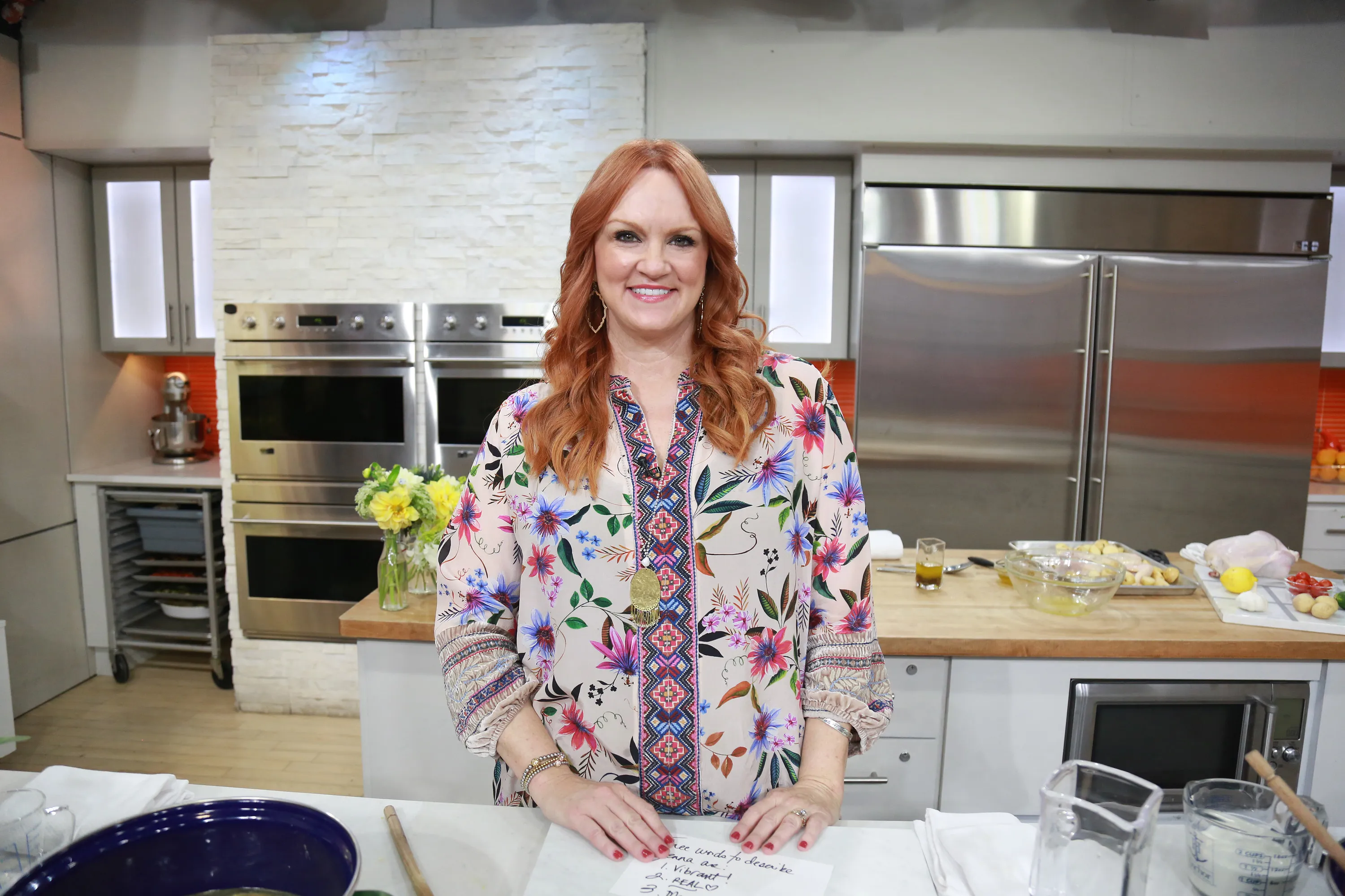 Ree Drummond smiling in a kitchen, wearing a floral and patterned blouse.