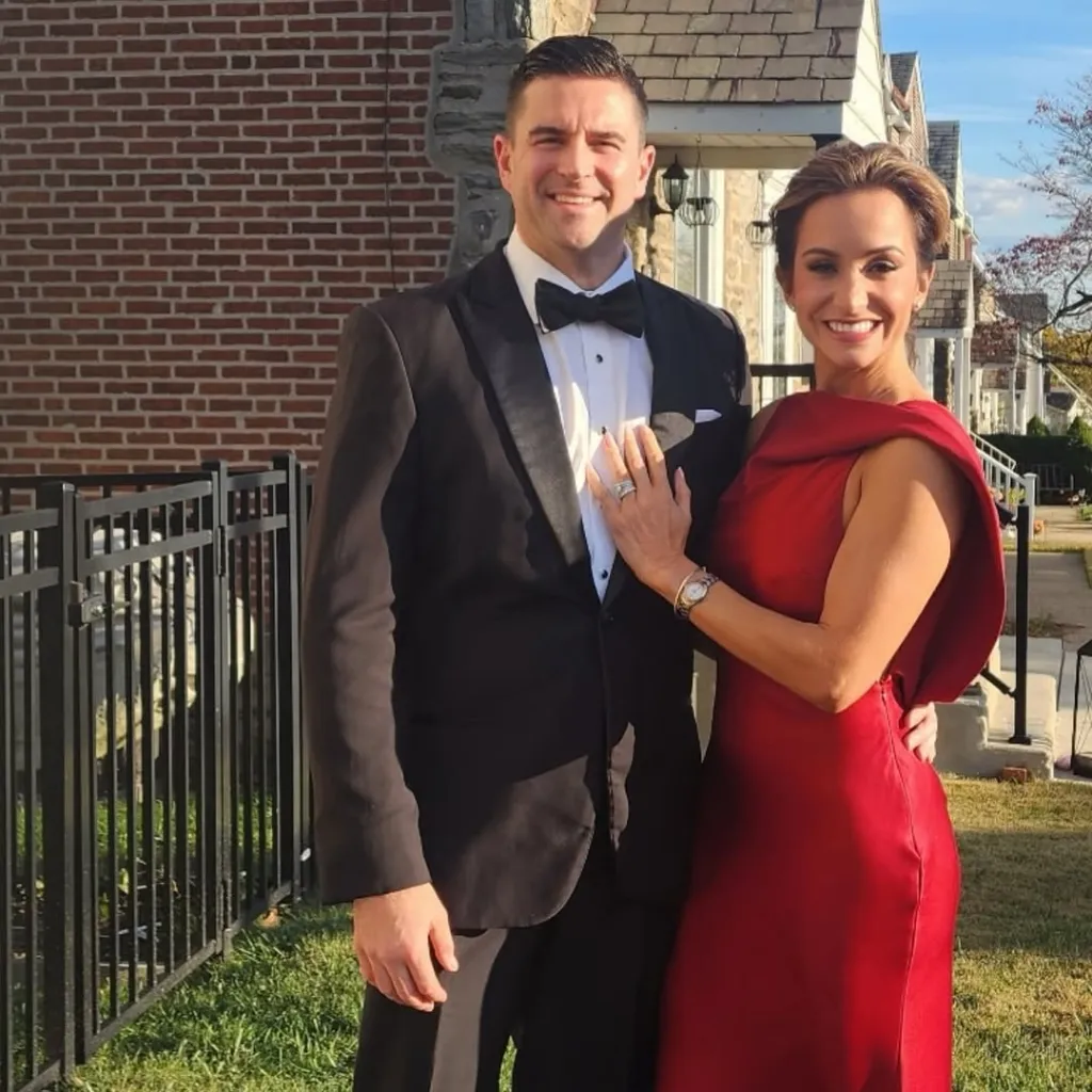 Dianna Russini and her husband, Kevin Goldschmidt, pose smiling while he wears a tuxedo and she wears a red dress.