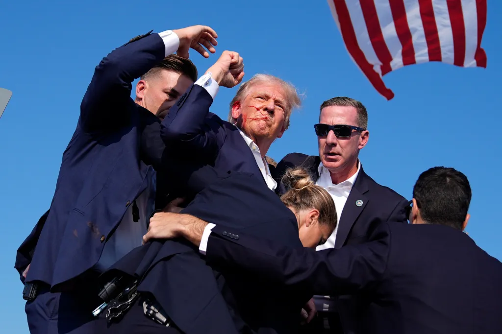 Former President Donald Trump is surrounded by Secret Service agents at a campaign rally, with blood visible on his face and ear.