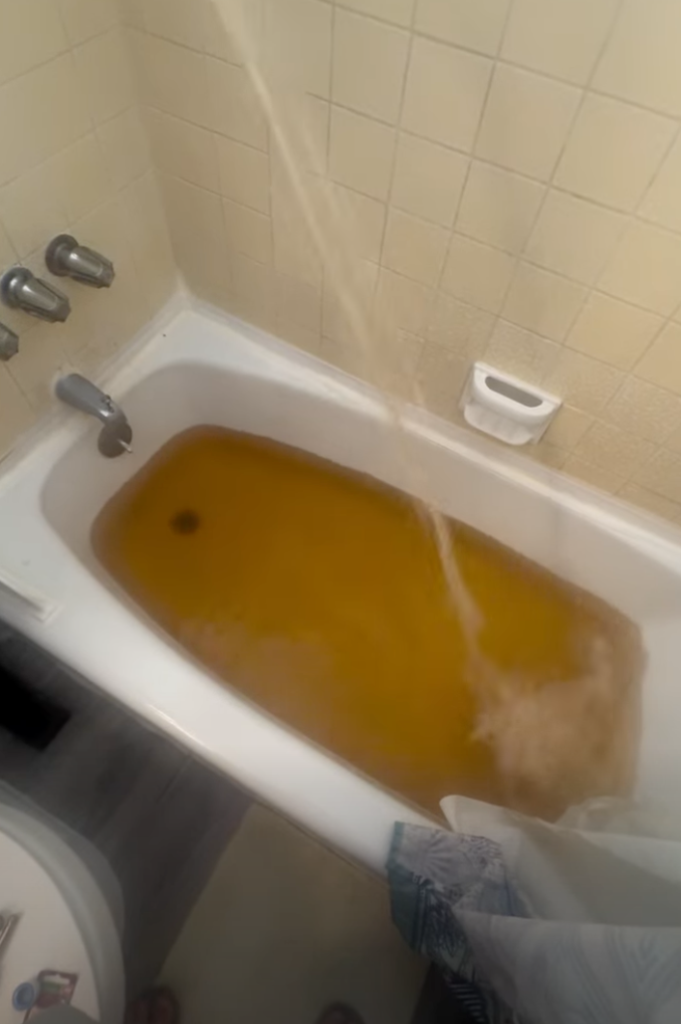 Bathtub full of brown tap water with more brown water streaming from the showerhead.