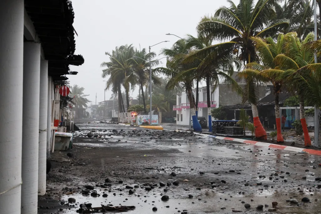Rain-swept street covered in rocks and debris from Hurricane Polo, with palm trees and buildings in the background.