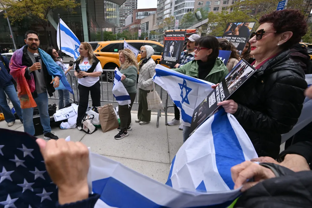 Rom El-Hai, a survivor of the Nova Music Festival attack, speaks to a crowd holding Israeli flags and signs that say