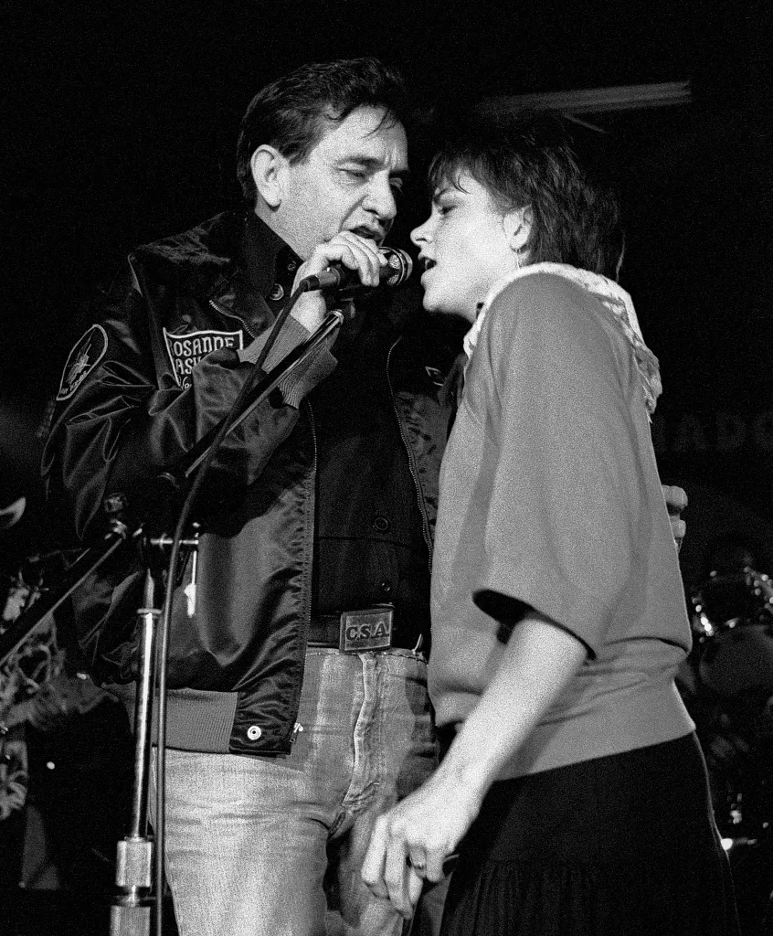 Johnny Cash and Rosanne Cash sing into a microphone on stage.