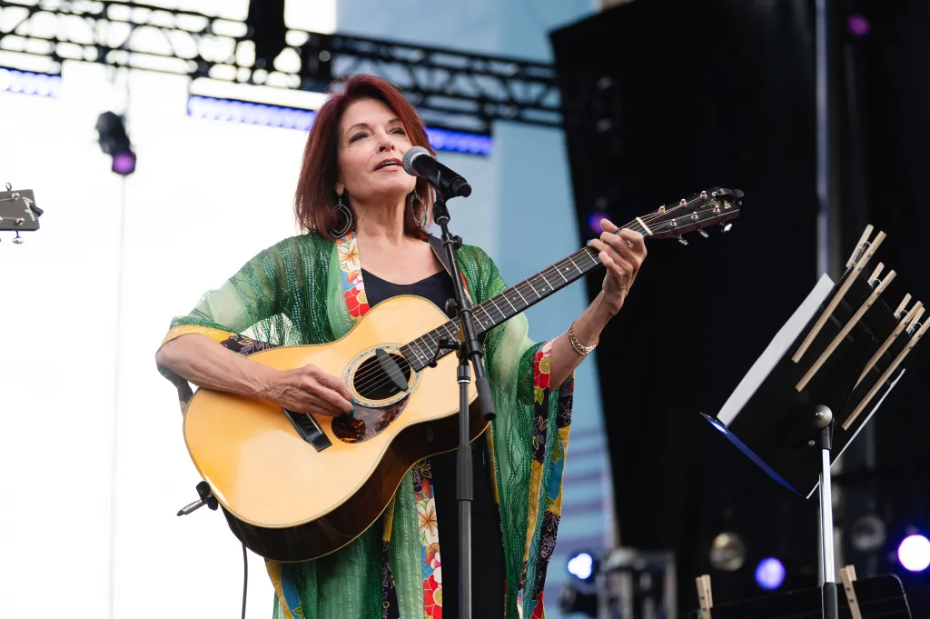 Rosanne Cash singing and playing an acoustic guitar on stage.