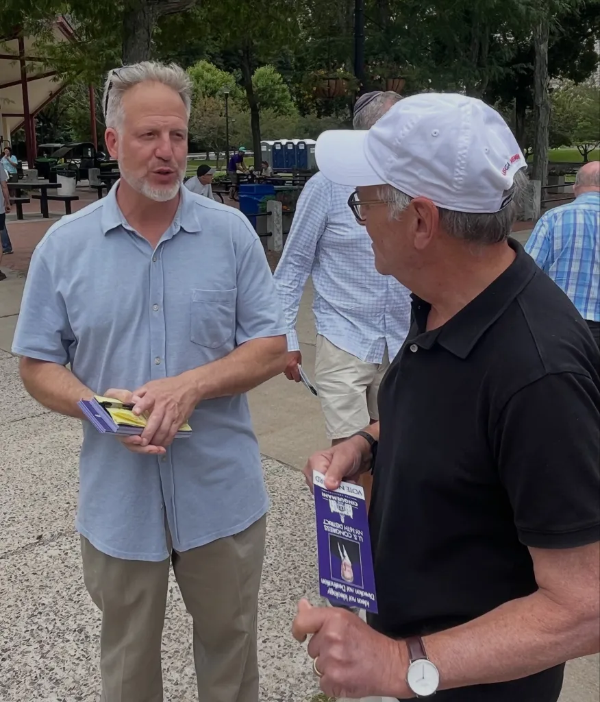 Joseph Cinquemani holding campaign literature while speaking to a man in a white hat.