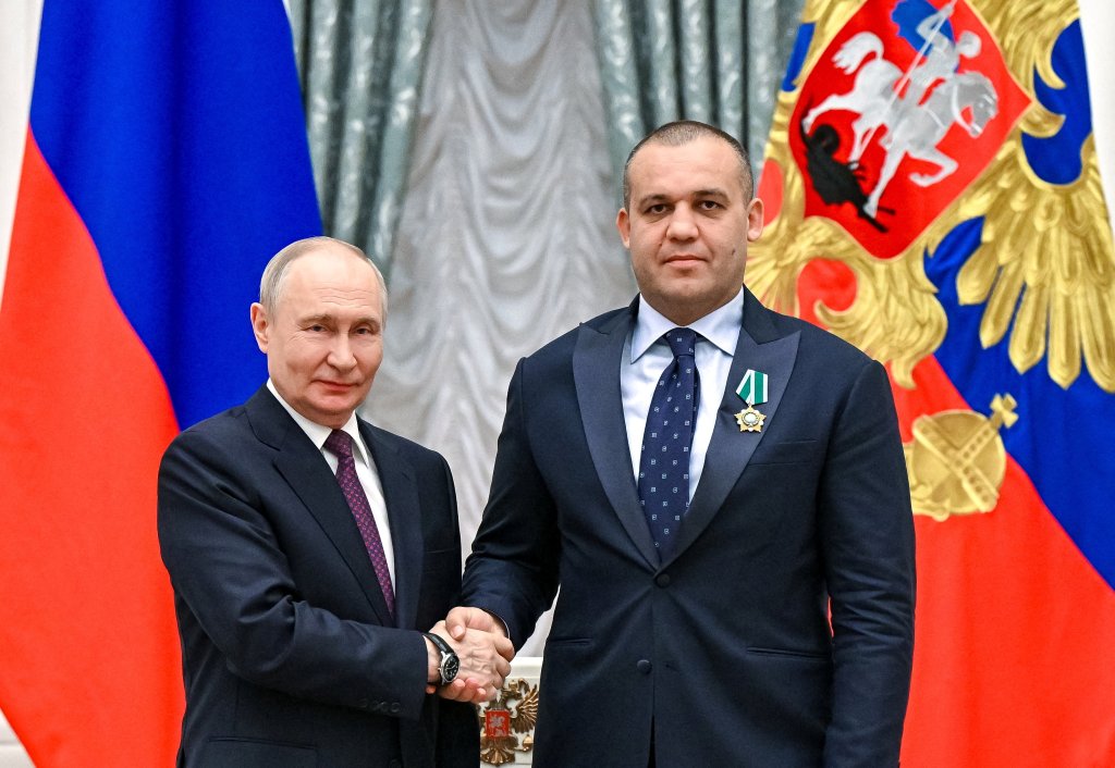 Russian President Vladimir Putin shaking hands with Umar Kremlev, chairman of the Russian Boxing Federation, who is wearing the Order of Friendship medal.