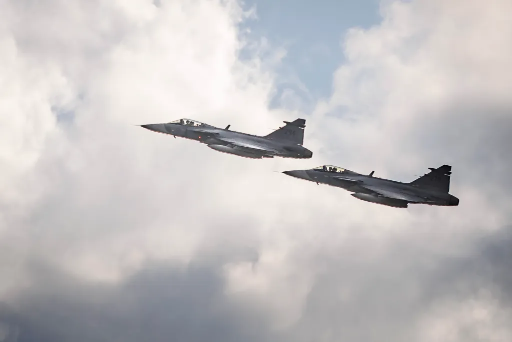Two Saab JAS 39 Gripen fighter jets flying in formation against a cloudy sky.
