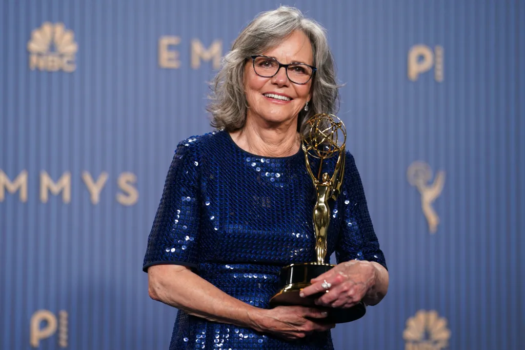 Sally Field in a sequined blue dress, smiling and holding an Emmy award.