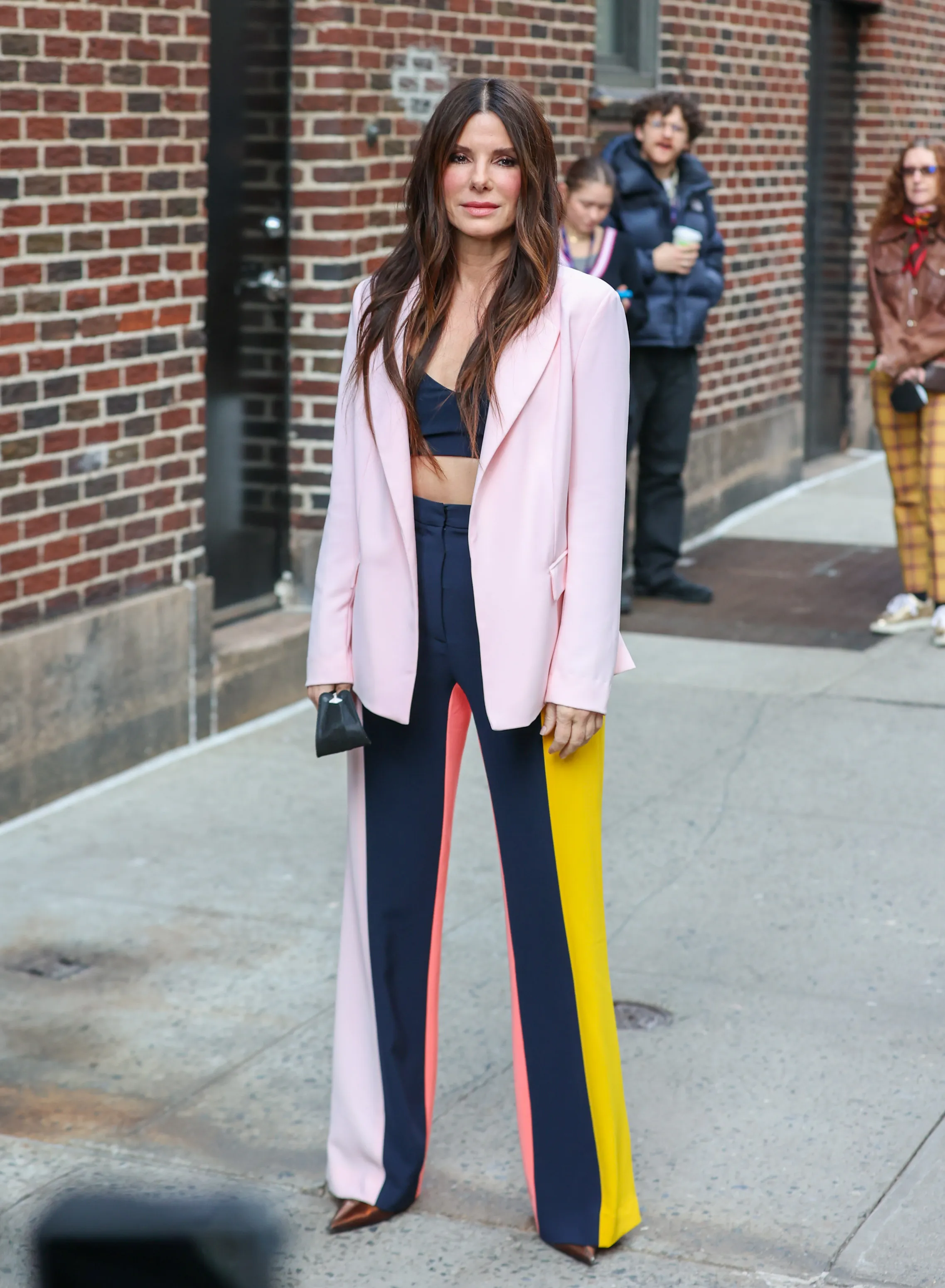 Sandra Bullock posing in a pink blazer, a navy blue crop top, and multi-colored pants.
