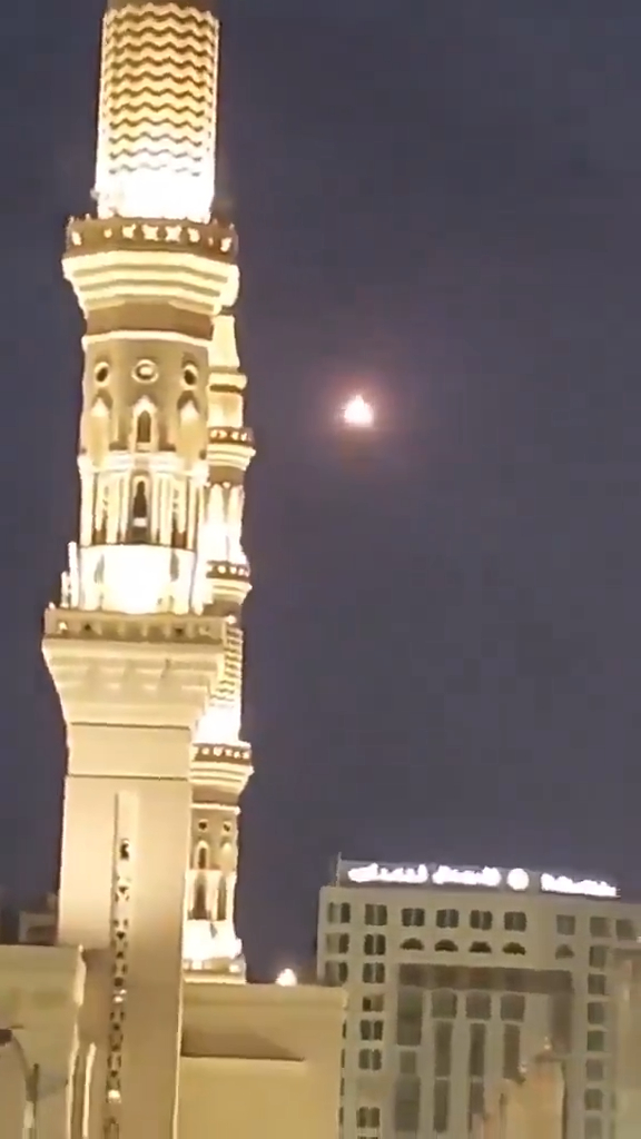 Saudi air defenses downed a drone over Mecca, shown with a bright light in the night sky next to a lit minaret.