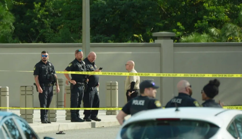 Police officers and investigators are gathered behind yellow 