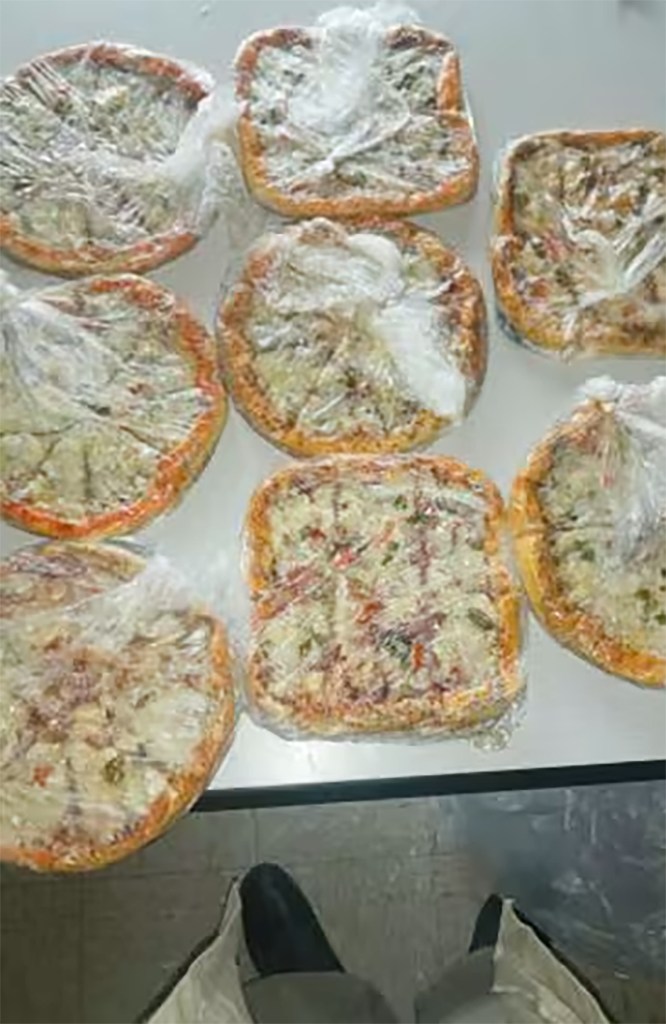 Several pizzas wrapped in plastic bags sitting on a table.