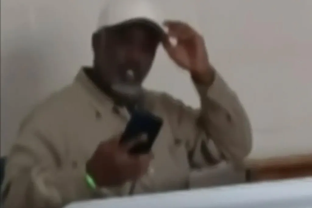 Sean Combs adjusting his hat while holding a phone in a correctional facility.
