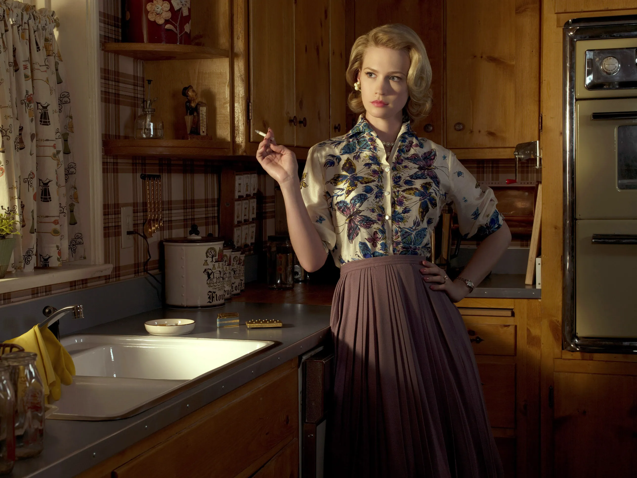 January Jones as Betty Draper smoking in a kitchen.