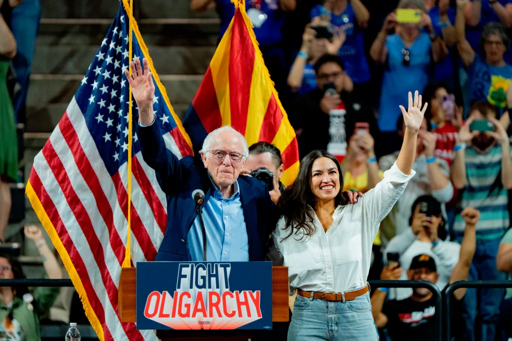 Sen. Bernie Sanders and Rep. Alexandria Ocasio-Cortez wave to supporters at a rally.