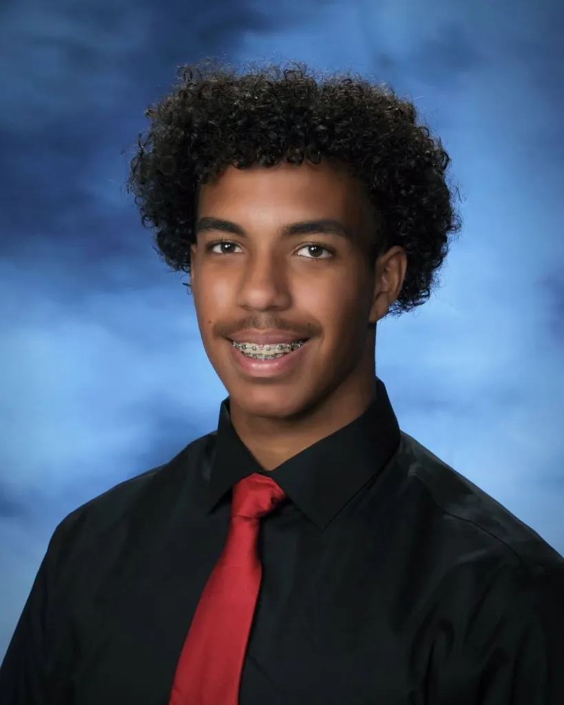 Headshot of Anthony Blas, a senior attending CSU Fullerton in the fall, wearing a black shirt and red tie against a blue background.