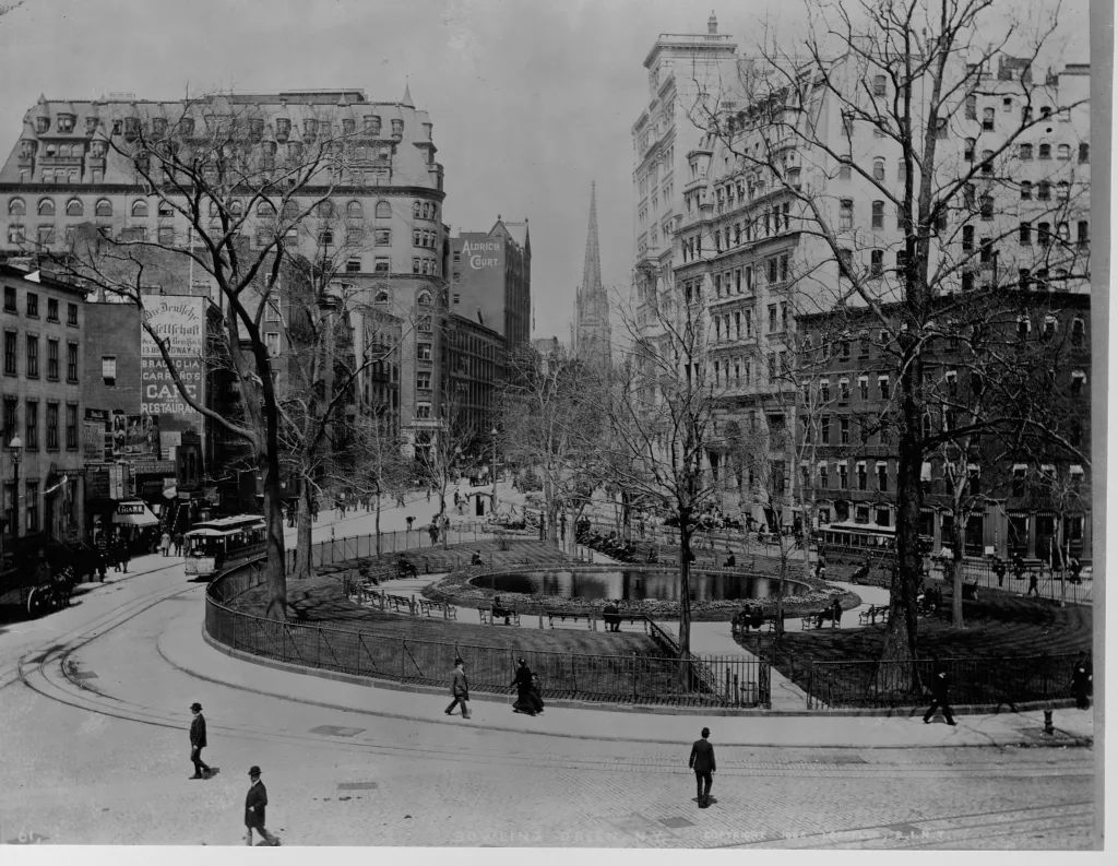 Pedestrians and streetcars move around Bowling Green park in Manhattan.