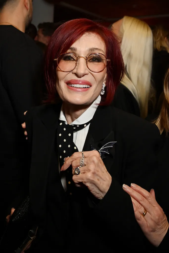 Sharon Osbourne in a black suit with a polka dot tie and a sparkling bat-wing brooch.