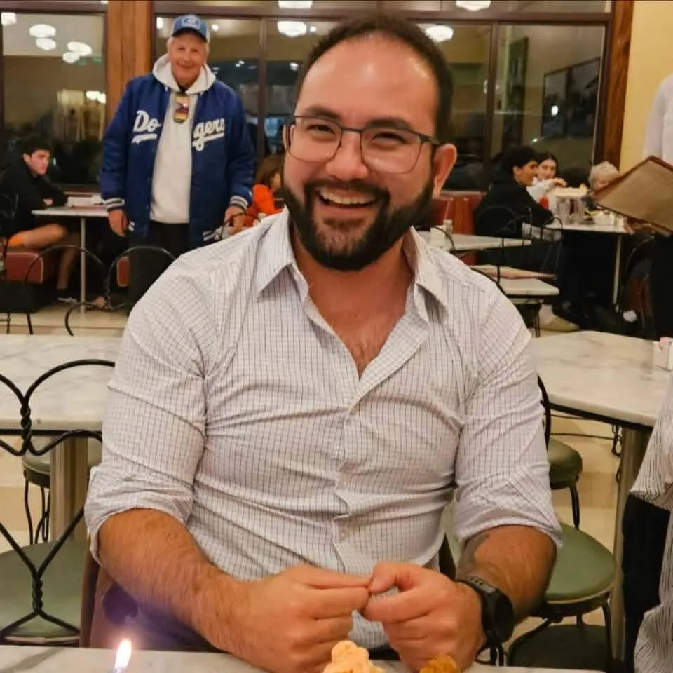 Jonathan McKinsey, a man with a beard and glasses, smiles while seated at a table.