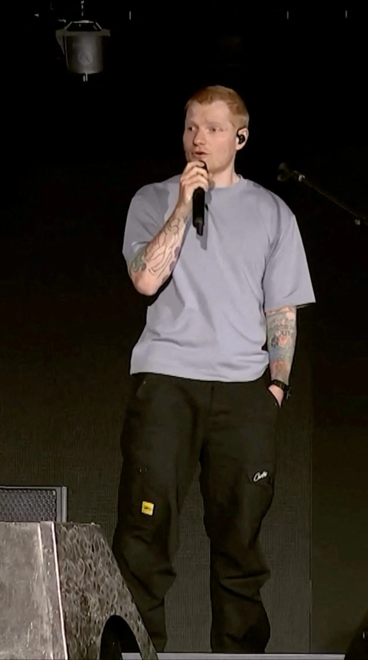 Singer Ed Sheeran holding a microphone and addressing the audience during a show.