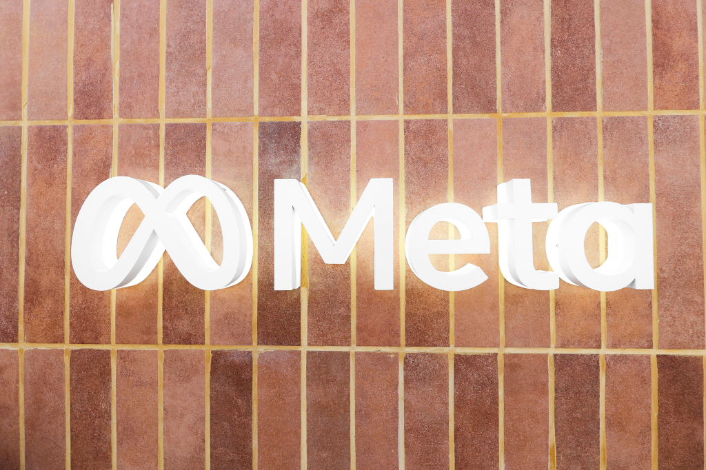 The white Meta corporate logo with a glowing halo, set against a brown tiled wall at the Fira Gran Via booth.
