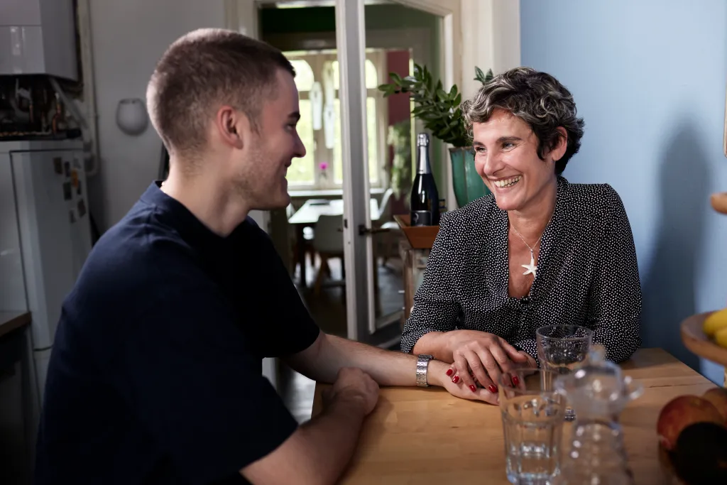 A smiling woman holds the hand of her adult son at home.